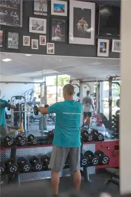 A Personal Touch Fitness coach doing cable work on the gym floor beside the dumbbell racks