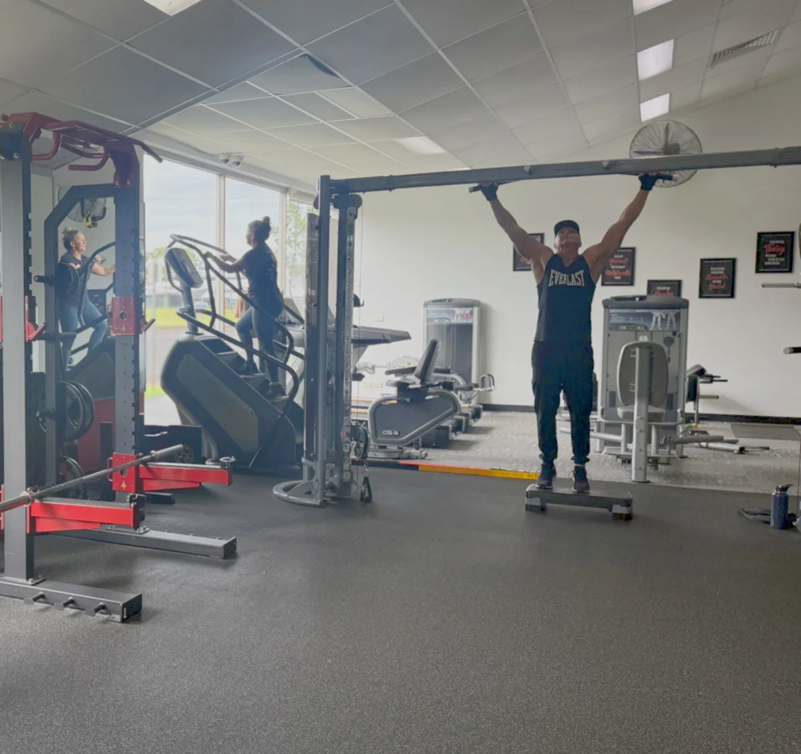 A member training on the pull-up bar beside the stair climber and squat rack at Personal Touch Fitness